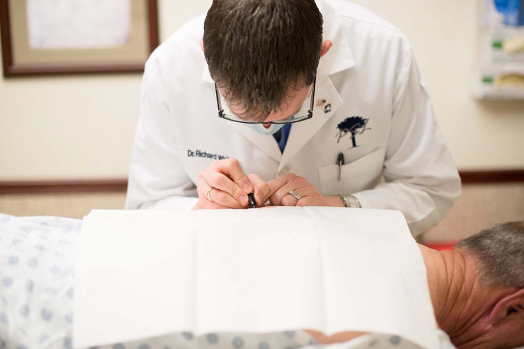 Doctor performing skin inspection on back of male patient