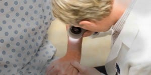 Doctor looking through magnifier examining skin on arm